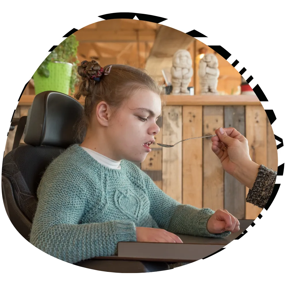 Disabled girl being fed with spoon by support worker